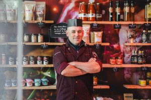 Boucher souriant devant des étagères de produits dans la Boucherie de la Venoge